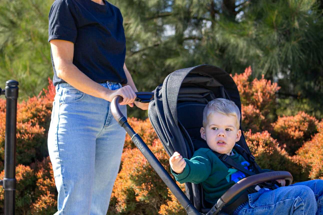 Woman pushing a stroller with a child inside, surrounded by greenery